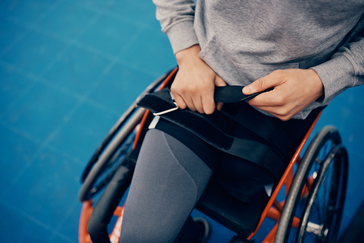 Unrecognizable athlete fastening belt on wheelchair while preparing to exercise on an outdoor court.